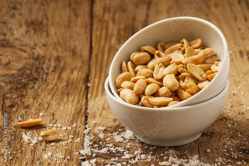 Roasted peanuts and salt in a bowl on a wooden background, selec