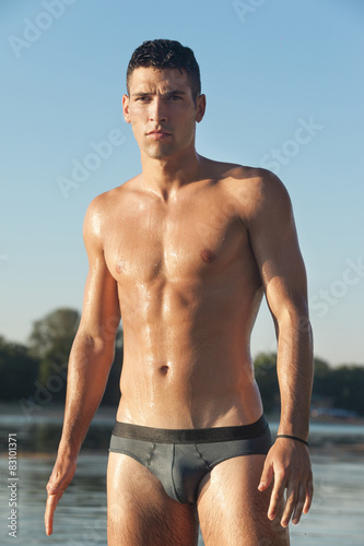 Muscular man in swim briefs getting out of water