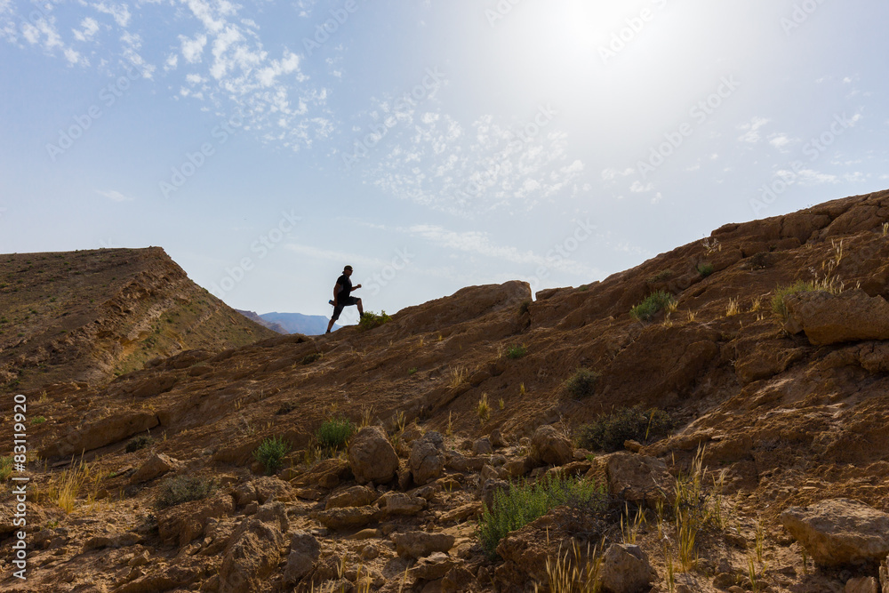 Spotsman running up stone desert hill.