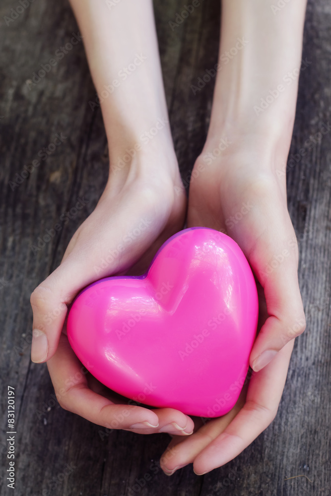 Obraz premium Beautiful female hands holding pink plastic heart over old woode