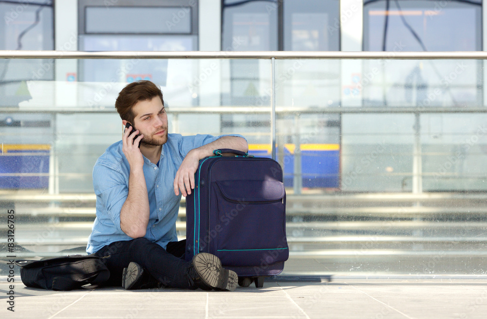 Male traveler sitting on floor talking on mobile phone