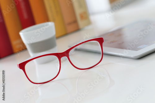 Red eyeglasses set on table by digital tablet