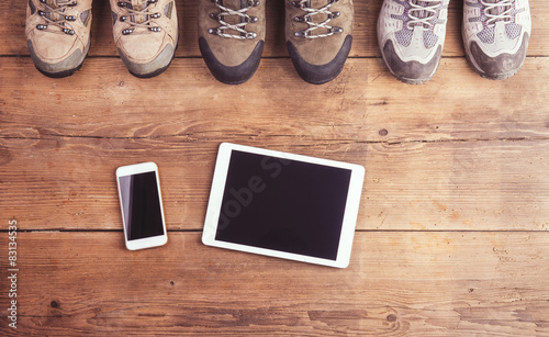 Hiking shoes, tablet and smart phone on a wooden background