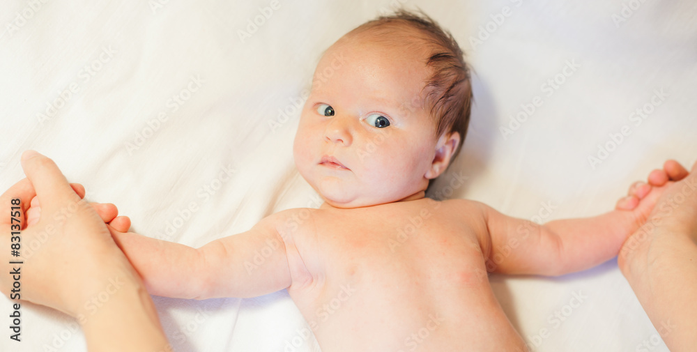 Mother makes baby stretching with happy newborn at white bed Mother makes baby stretching with happy newborn at white bed