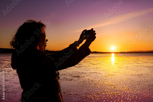 Woman taking selfie on a beach during sunset.