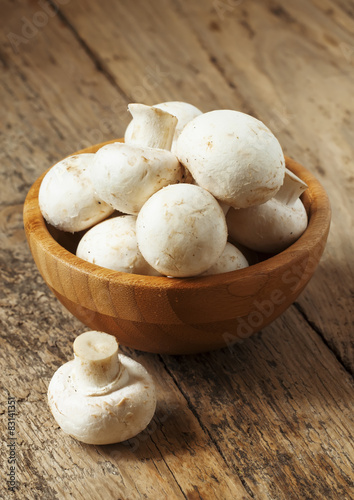 White mushrooms in a bowl on wooden table, selective focus