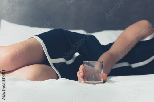 Young woman lying on bed with glass in her hand