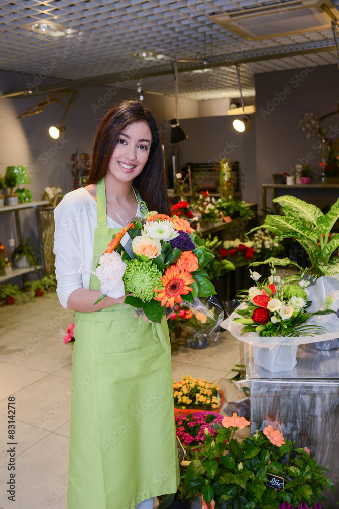 Fototapeta premium cheerful young woman florist selling flowers in flower shop