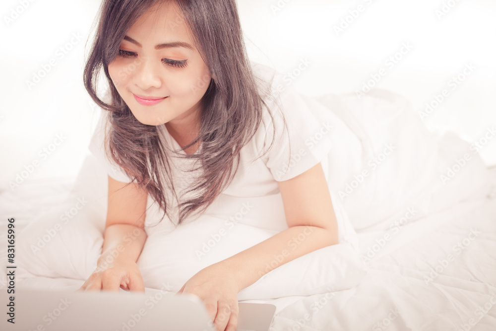Smiling woman using a laptop while lying on her bed Smiling woman using a laptop while lying on her bed