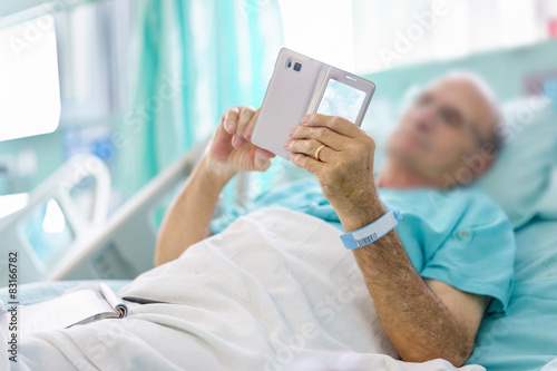 Mature male patient playing a mobile on bed in hospital