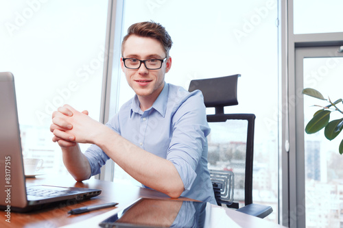 Young smiling man sitting at desk in office 