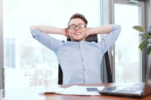 Businessman at desk with hands behind his head 