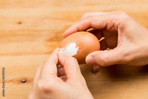 Fingers peeling hard boiled egg on wooden table