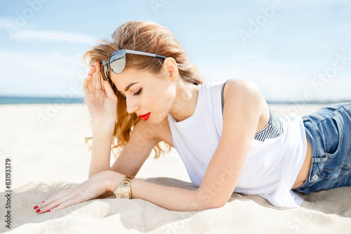 Attractive girl in sunglasses posing lying on the sea beach 