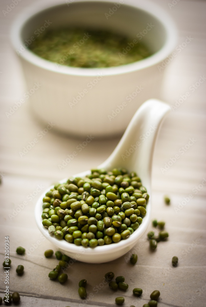 Raw mung beans in ceramic spoon over white wooden background Raw mung beans in ceramic spoon over white wooden background