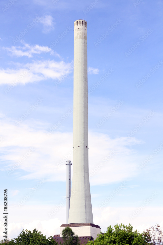 a high concrete chimney with white smoke clouds blue sky