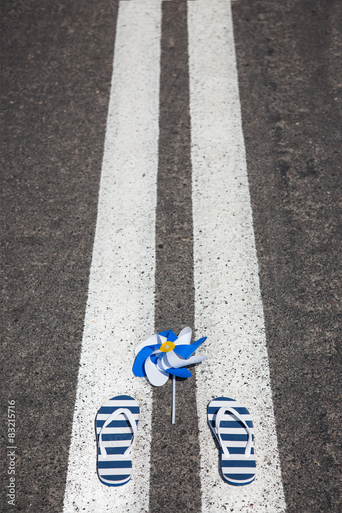 Fototapeta premium Beach slippers with pinwheel lying on grey asphalt