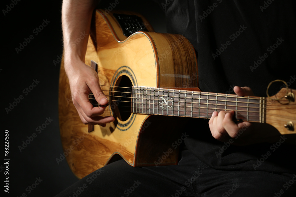 Young man playing on acoustic guitar on dark background