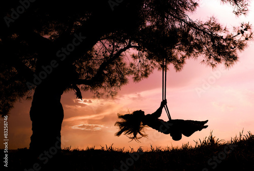 silhouette of happy young woman on a swing with sunset photo