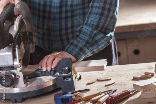 Close up of senior carpenter cutting wooden plank with circular saw in his workshop.