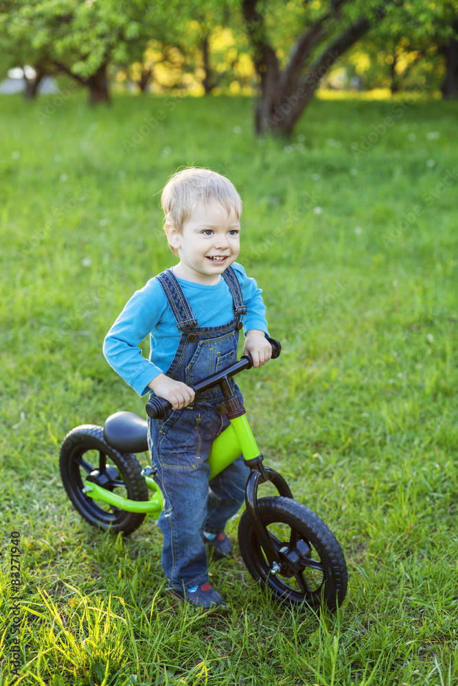 Happy little boy riding learner bike on grass