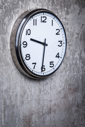 Round wall clock hanging on the grey concrete wall