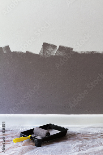 Half painted wall with roller and tray with space for text photo