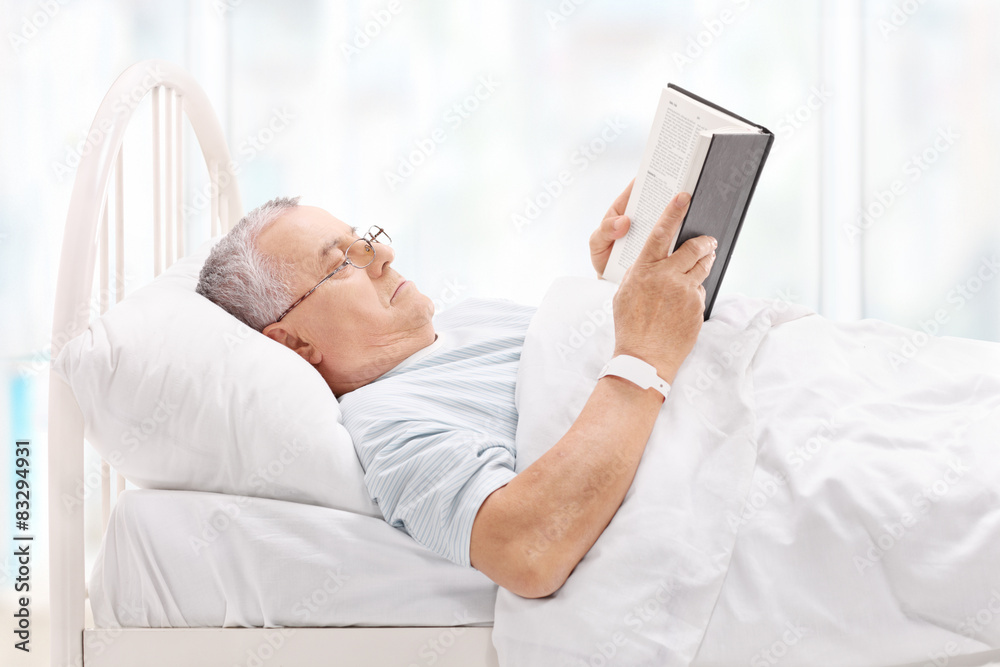 Mature patient lying in bed and reading a book