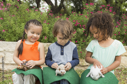 Three children seated in a row, each with a small animal on their lap. photo