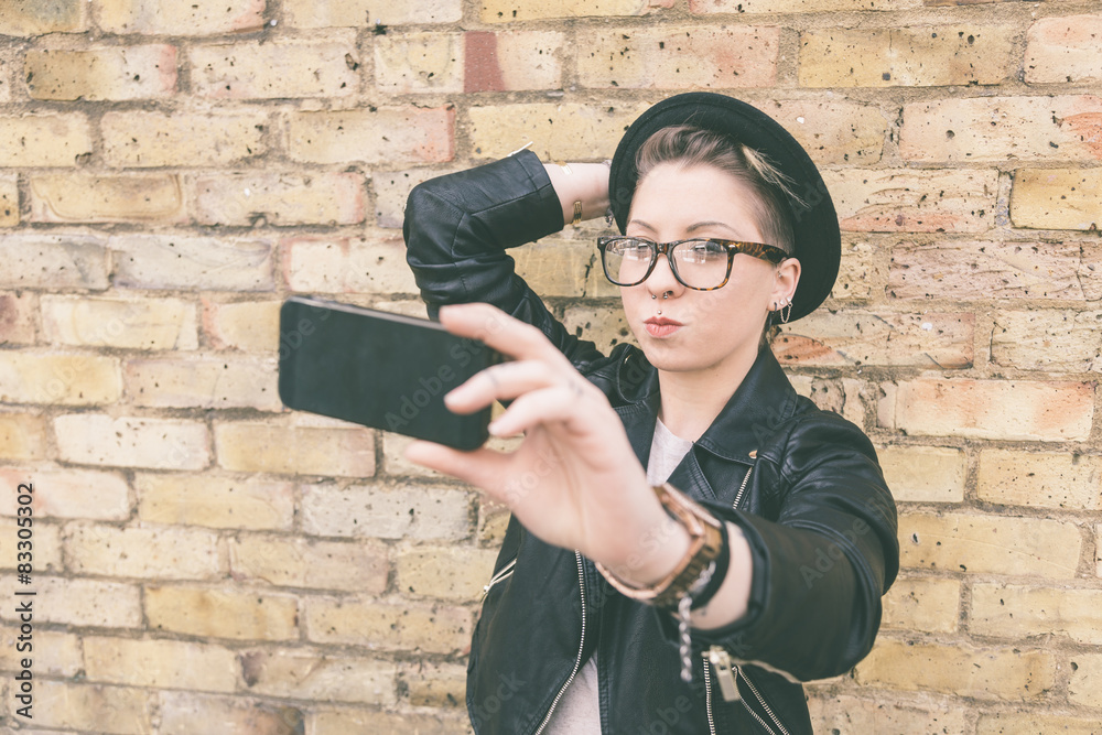 Hipster woman taking a selfie against brick wall in London. Hipster woman taking a selfie against brick wall in London.