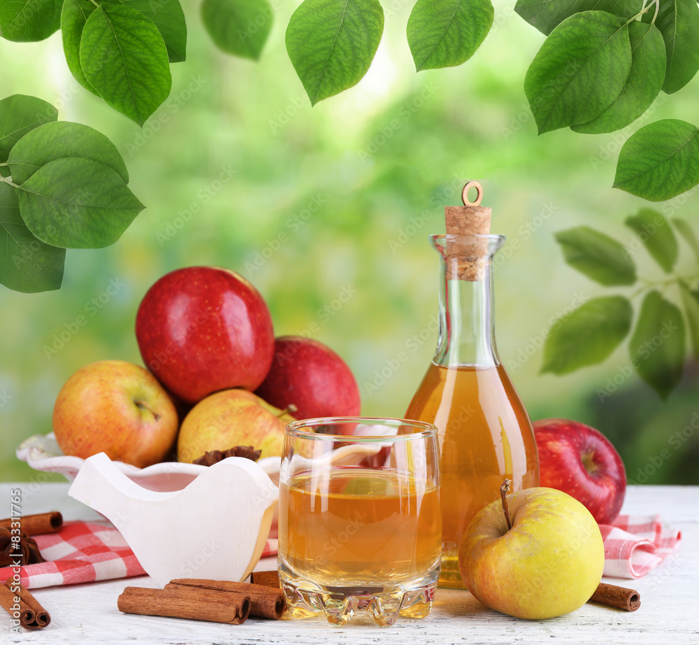 Apple cider in bottle with cinnamon sticks and fresh apples on nature background