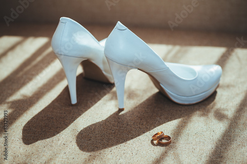 Two gold rings laying on white wedding bridal shoes