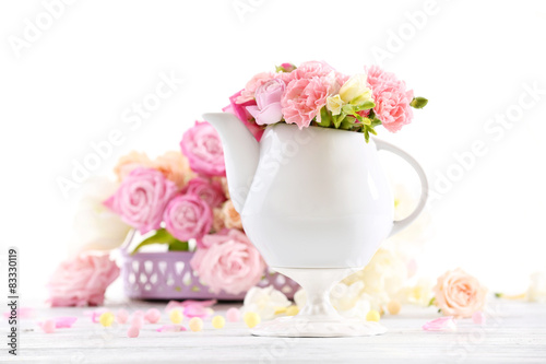 Composition with beautiful spring flowers in teapot on light pink background