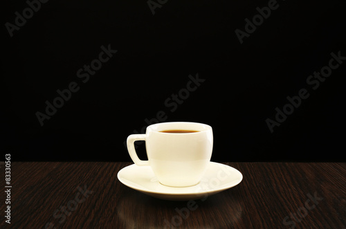 Cup of coffee on wooden table, on dark background