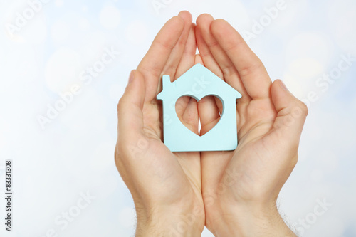 Female hands holding house on light blurred background