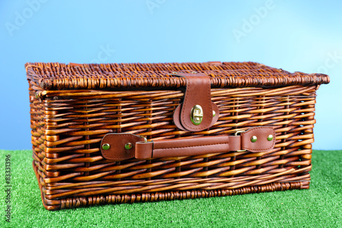 Wicker picnic basket on green grass on blue background