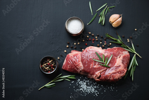 Fotografie Above view of raw ribeye steak with spices over black background