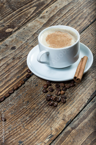 Cup of coffee on amid whole coffee beans with cinnamon