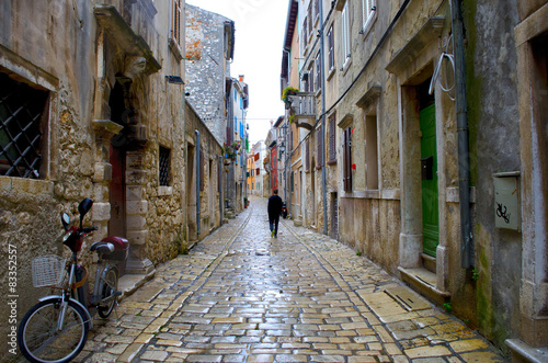 Fototapeta Naklejka Na Ścianę i Meble -  A lonely man walking along a narrow italian medieval street full of closed shops in an early sunday morning