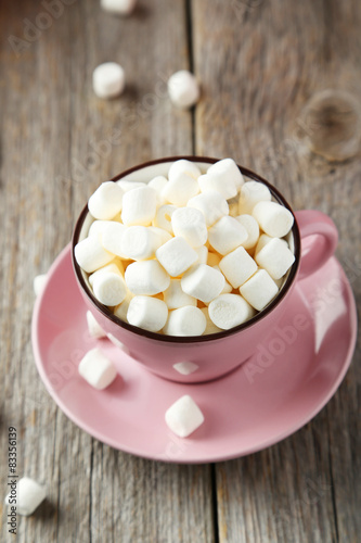 Marshmallows in pink cup on grey wooden background