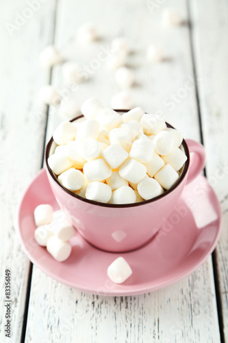 Marshmallows in pink cup on white wooden background