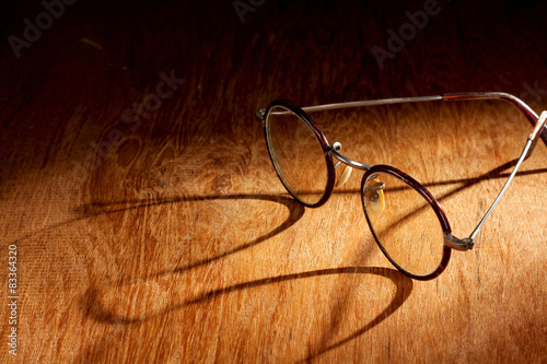 Spectacles with long shadow on wooden surface photo