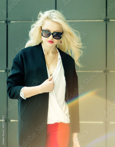 Beautiful business woman in trendy sunglasses over black wall. photo