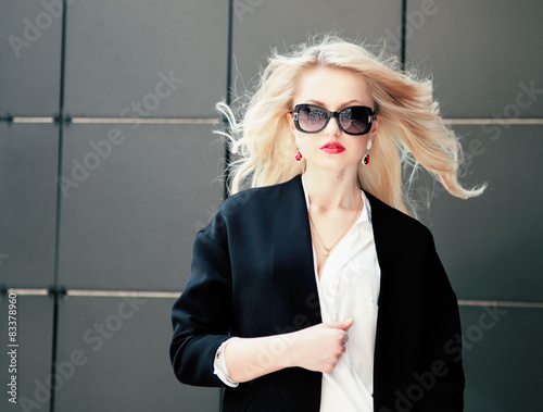 Beautiful business woman in trendy sunglasses over black wall. photo
