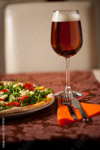 Pizza with rucola, cherry tomatoes and a glass of beer on a tebl