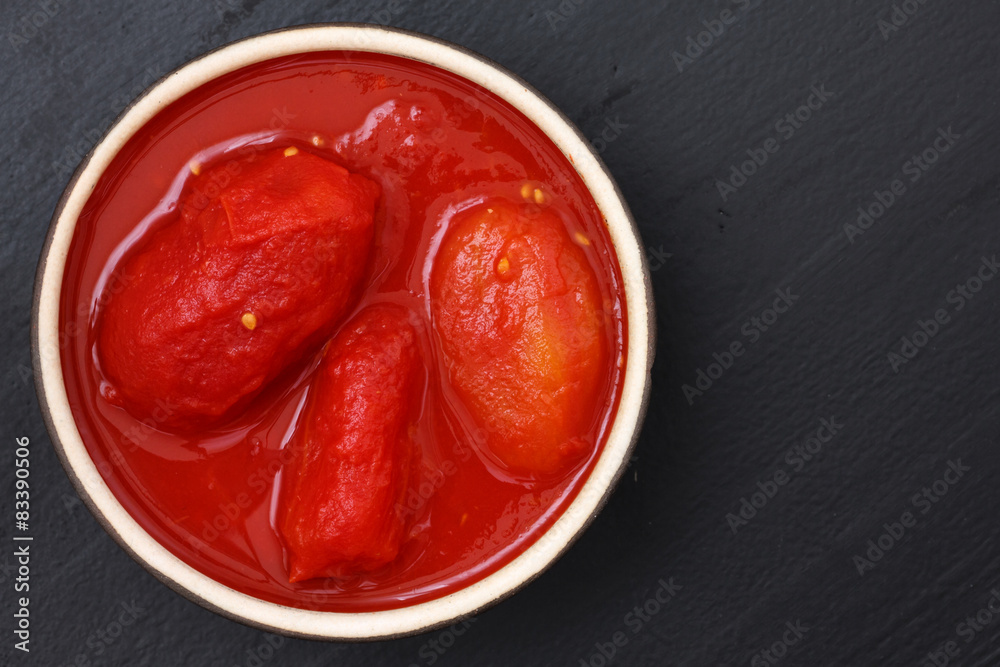 Whole canned tomatoes in dish from above on black wood.