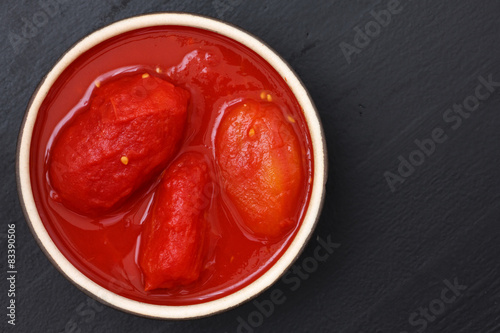 Whole canned tomatoes in dish from above on black wood.
