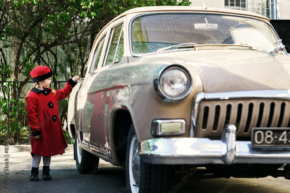 Cute little girl dressed in retro coat posing near oldtimer car