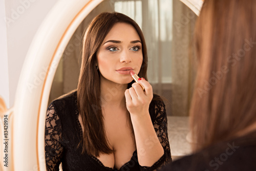 sexy girl sitting at a mirror and paints her lips lipstick