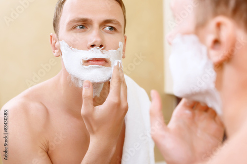 Topless man applying mean of shaving on face 